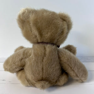 Brown teddy bear sitting on a white wooden surface with a white background