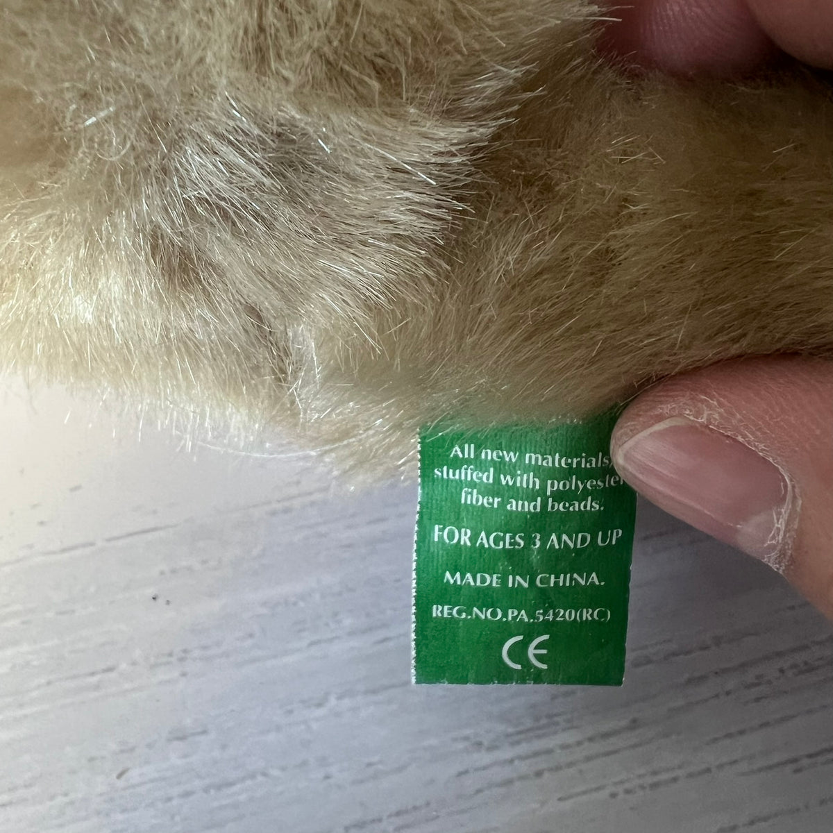 Close-up of a green label on a plush toy with a hand holding it.