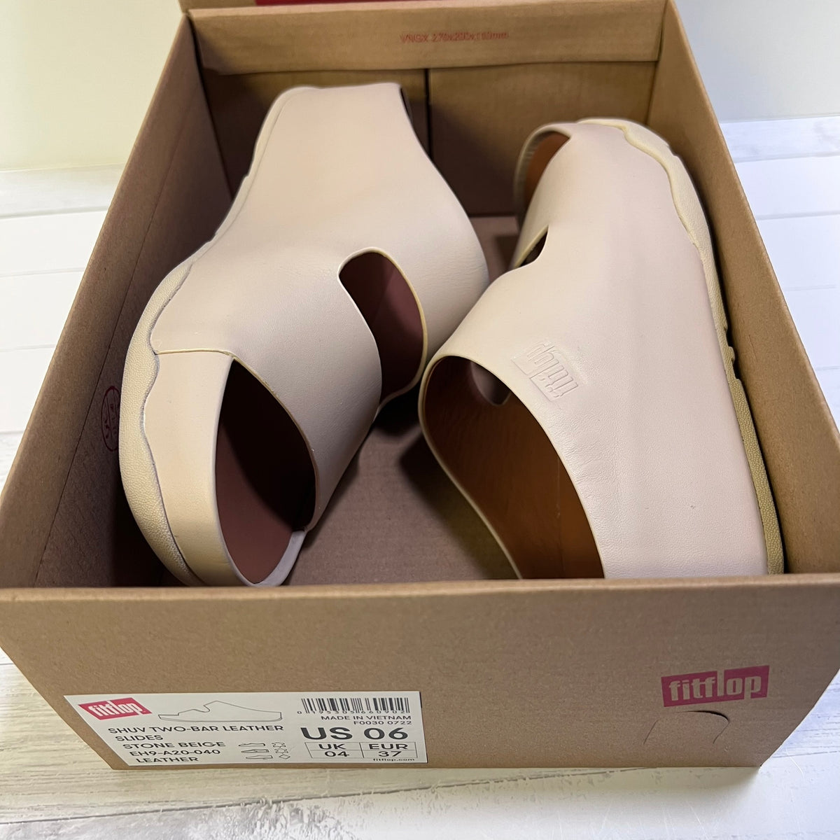 A pair of Fitflop platform slide sandals in light beige leather, shown inside their original brown cardboard shoebox. The Fitflop brand logo is visible on the box and embossed on the side of the shoe.