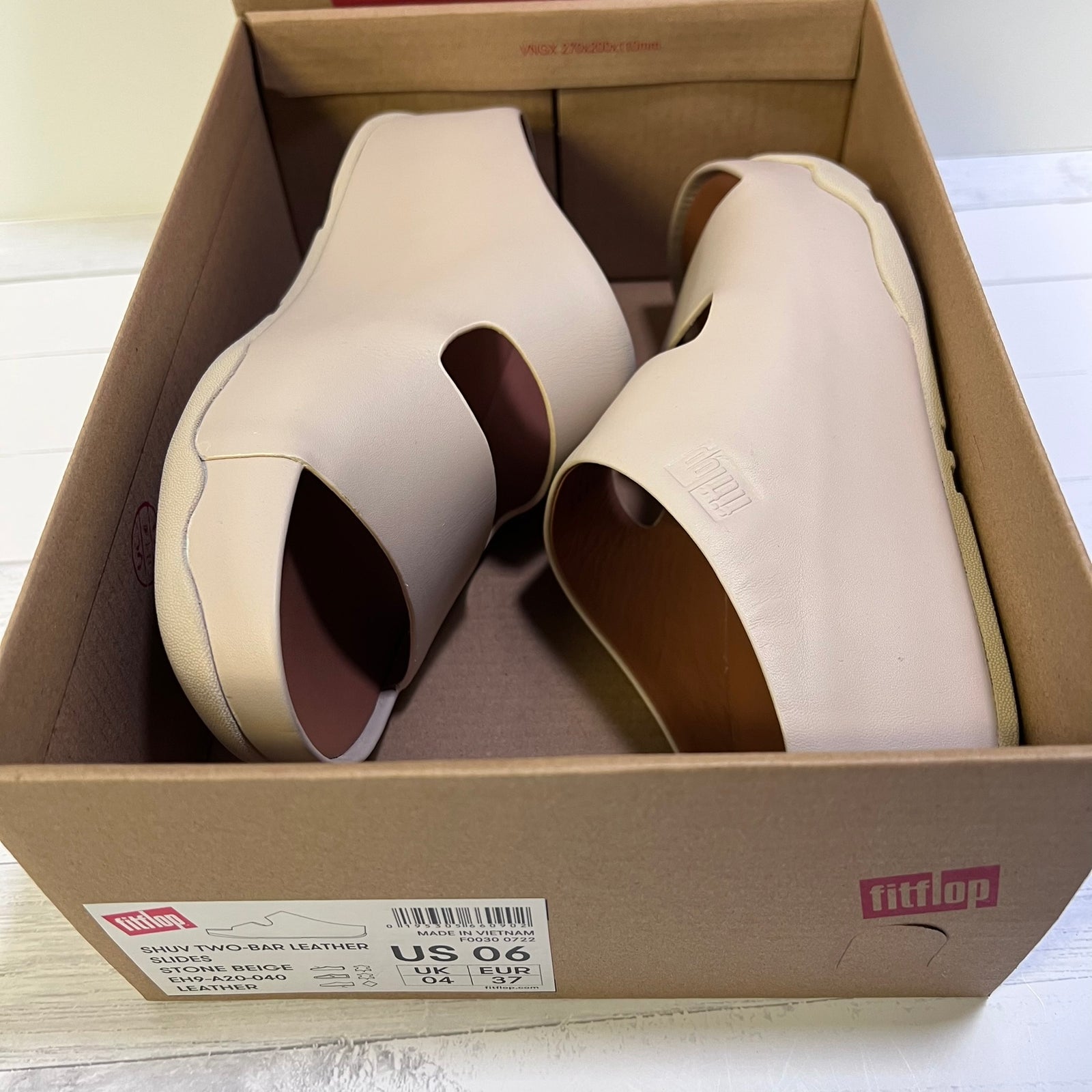 A pair of Fitflop platform slide sandals in light beige leather, shown inside their original brown cardboard shoebox. The Fitflop brand logo is visible on the box and embossed on the side of the shoe.
