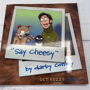Cartoon illustration of a dog and a person with text 'Say cheesy' by Darby Conley on a wooden surface.