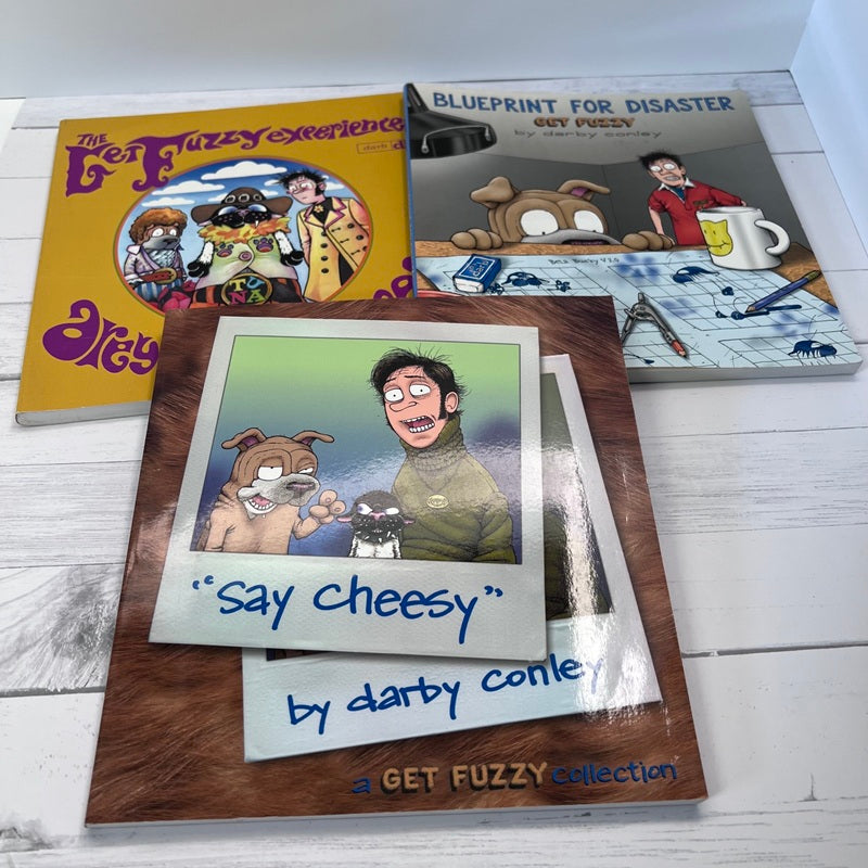 Collection of 'Get Fuzzy' books and prints on a wooden surface