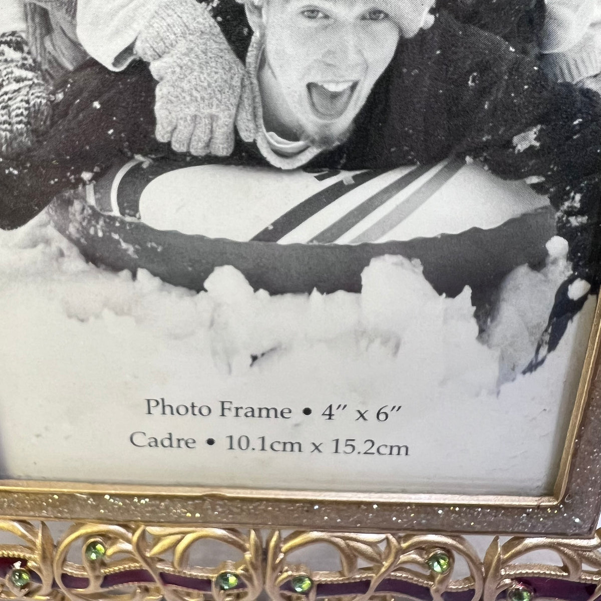 A close-up of a decorative photo frame with a black-and-white printed sample photo of a person in snow, plus printed size text reading 'Photo Frame 4" x 6"' and 'Cadre 10.1cm x 15.