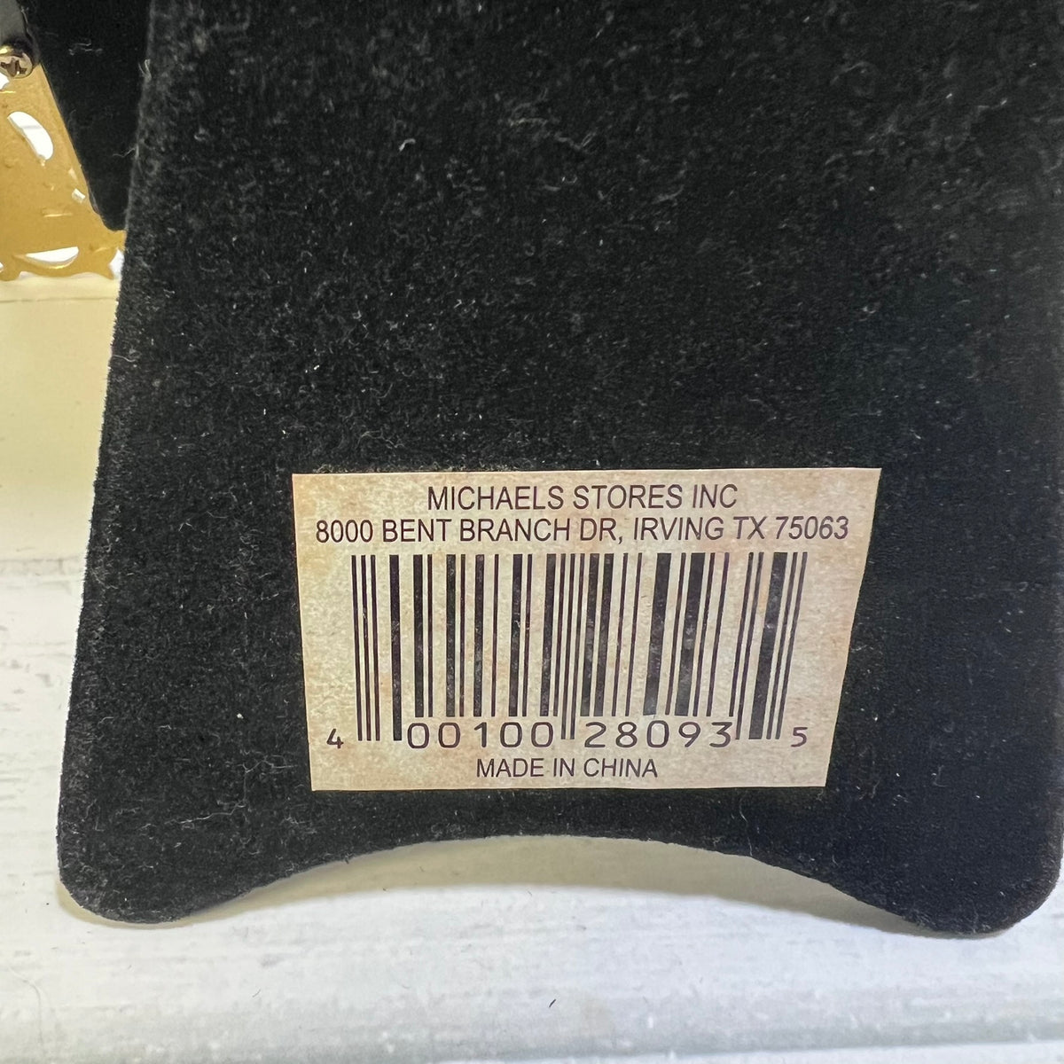 A close-up of a black velvet or felt surface with a beige barcode label reading 'MICHAELS STORES INC' and 'MADE IN CHINA'.
