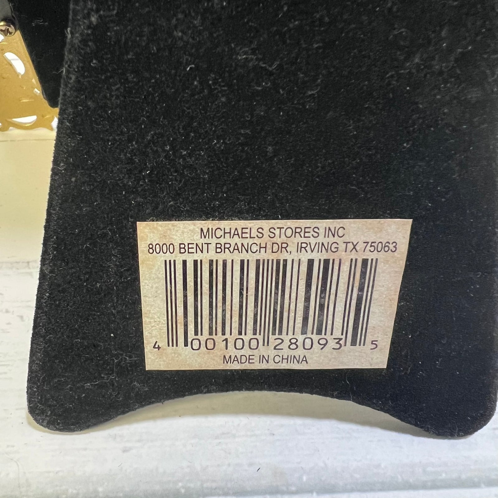 A close-up of a black velvet or felt surface with a beige barcode label reading 'MICHAELS STORES INC' and 'MADE IN CHINA'.