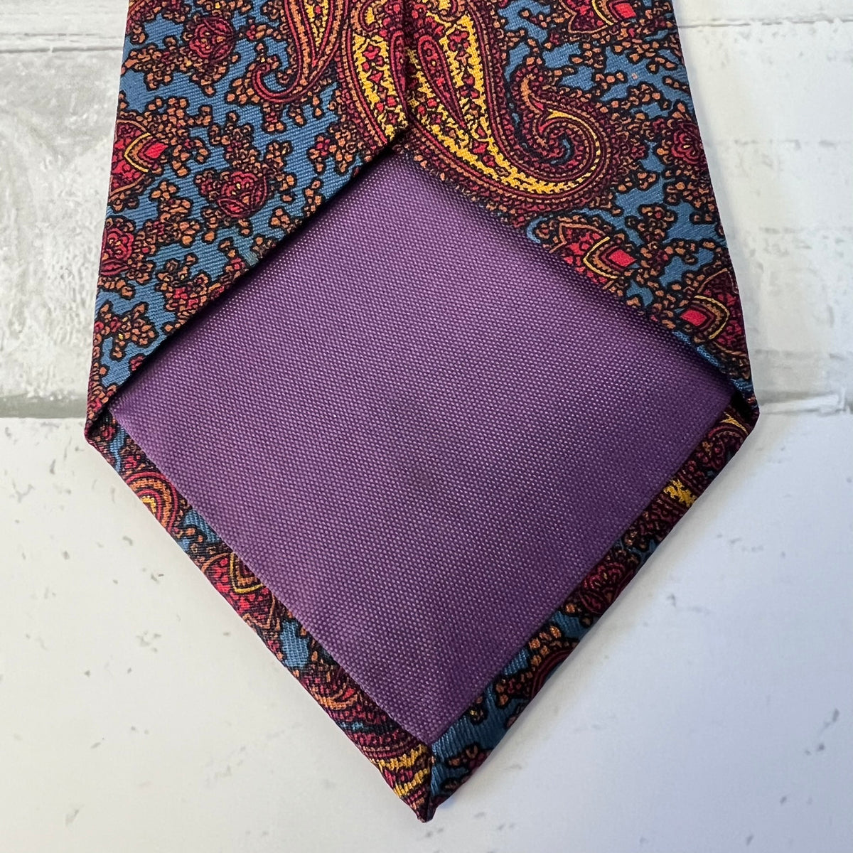 Purple pocket square with a patterned border on a light gray background