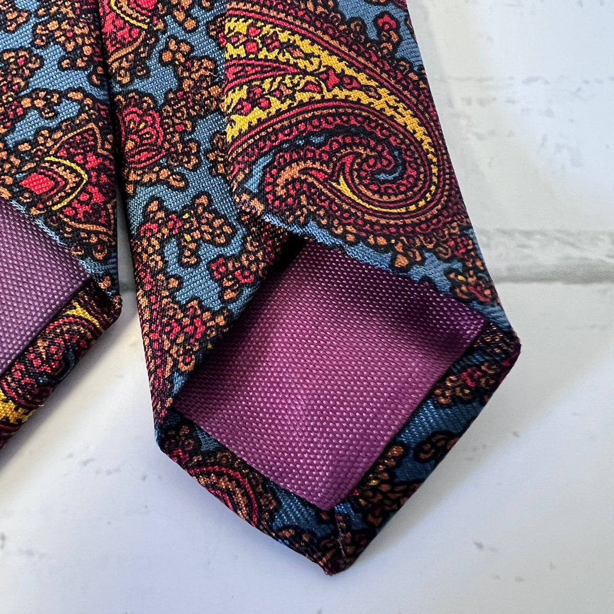 Colorful paisley tie with a matching pocket square on a white surface