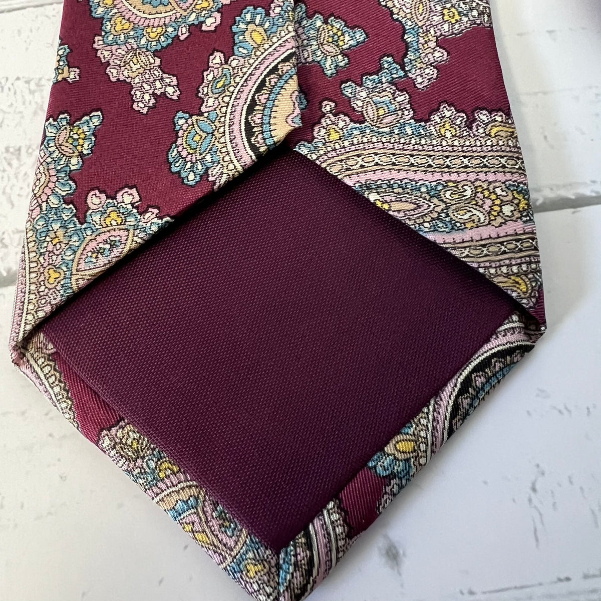Burgundy paisley tie and pocket square on a white surface