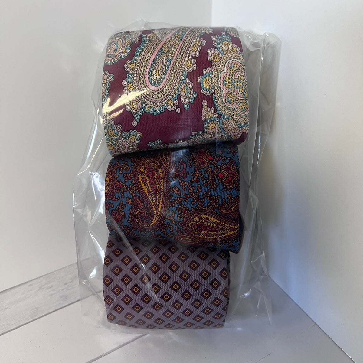 Two patterned ties in clear packaging on a white floor.