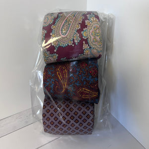 Two patterned ties in clear packaging on a white floor.