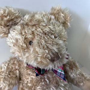 Beige teddy bear with a plaid bow tie on a white background