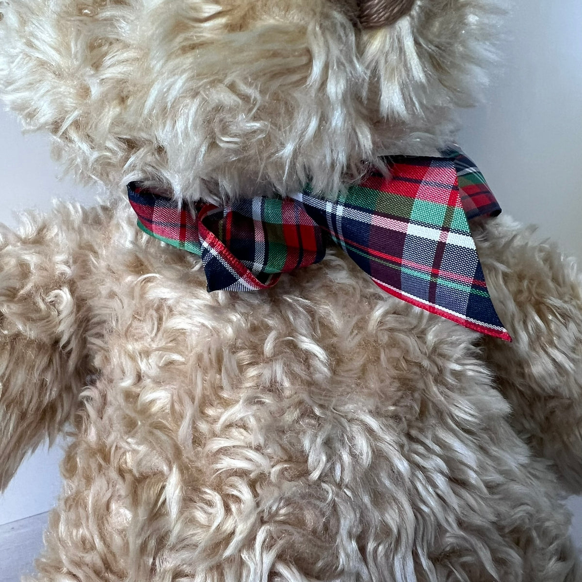 Beige teddy bear wearing a plaid bow tie on a white background