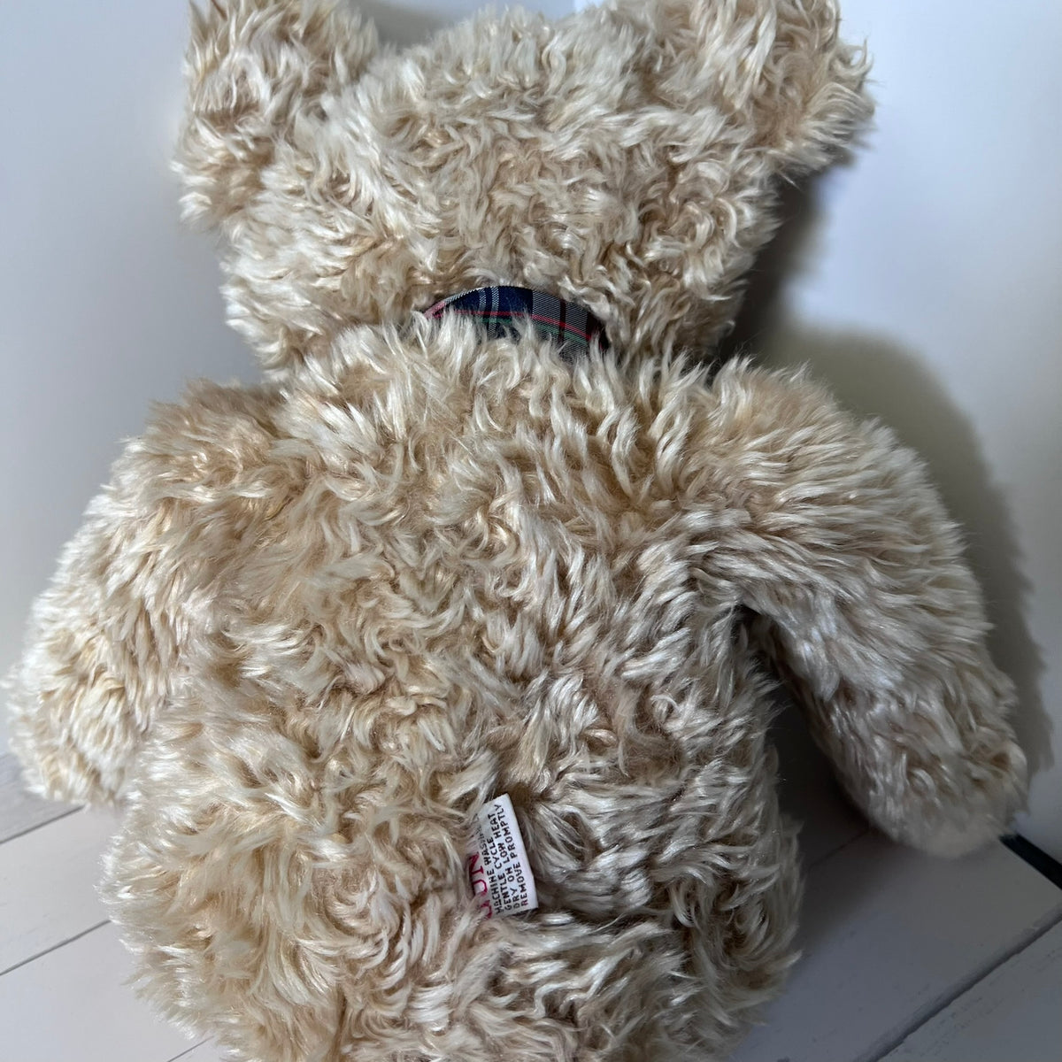 Beige teddy bear with a visible tag on a white surface