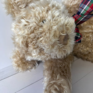 Close-up of a beige teddy bear with a plaid bow tie on a white floor.