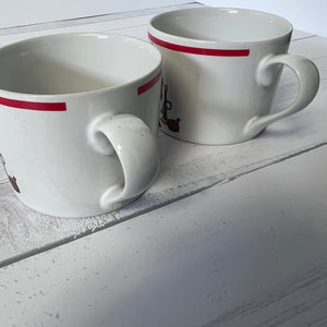 Two white mugs with red stripes on a light wooden surface