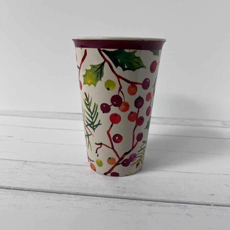 Decorative cup with holly design on a white wooden surface