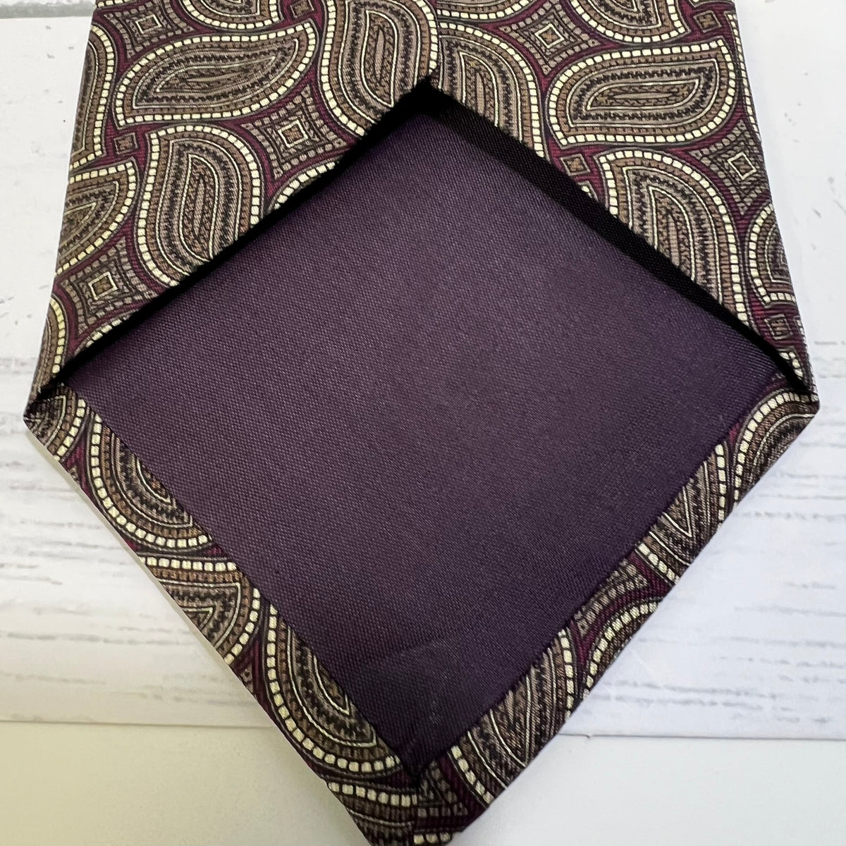 Purple pocket square with a patterned border on a white surface