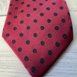 Red tie with black floral pattern on a light wooden surface
