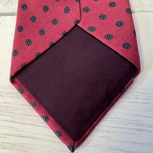 Red tie with black floral pattern and matching pocket square on a light background