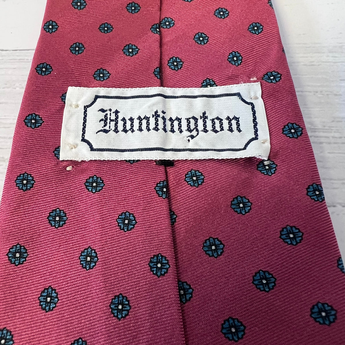 Red tie with black floral pattern and 'Huntington' label on a white background