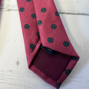 Folded burgundy tie with black floral patterns on a light wooden surface