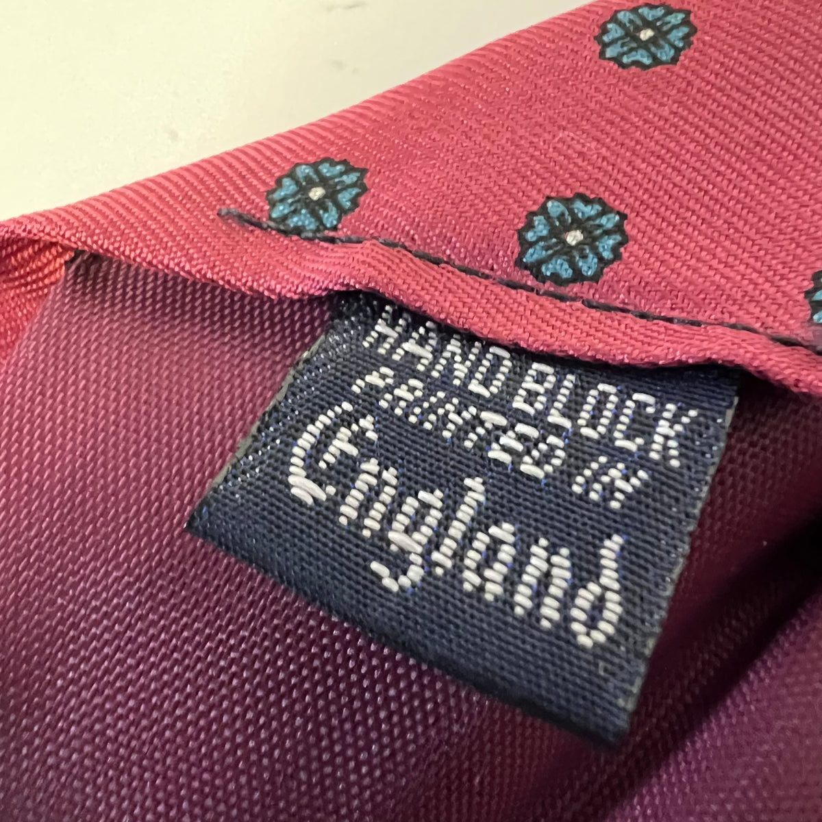 Close-up of a maroon fabric with a label stating 'Hand Block Printed in England'.