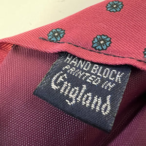 Close-up of a maroon fabric with a label stating 'Hand Block Printed in England'.