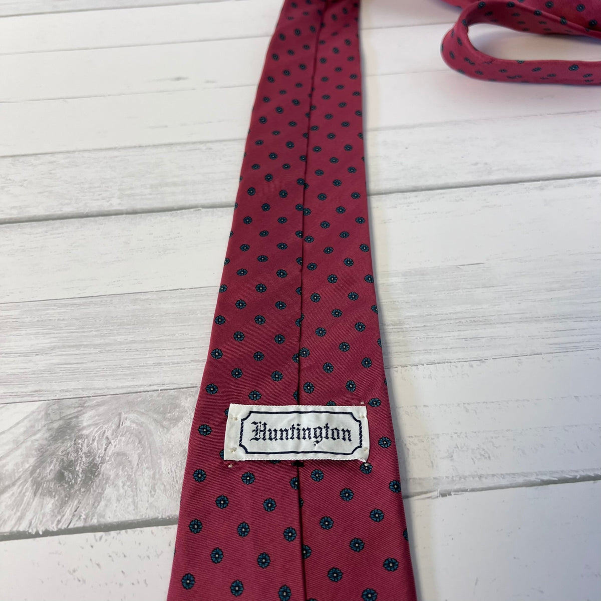 Red tie with black polka dots and 'Huntington' label on a light wooden surface