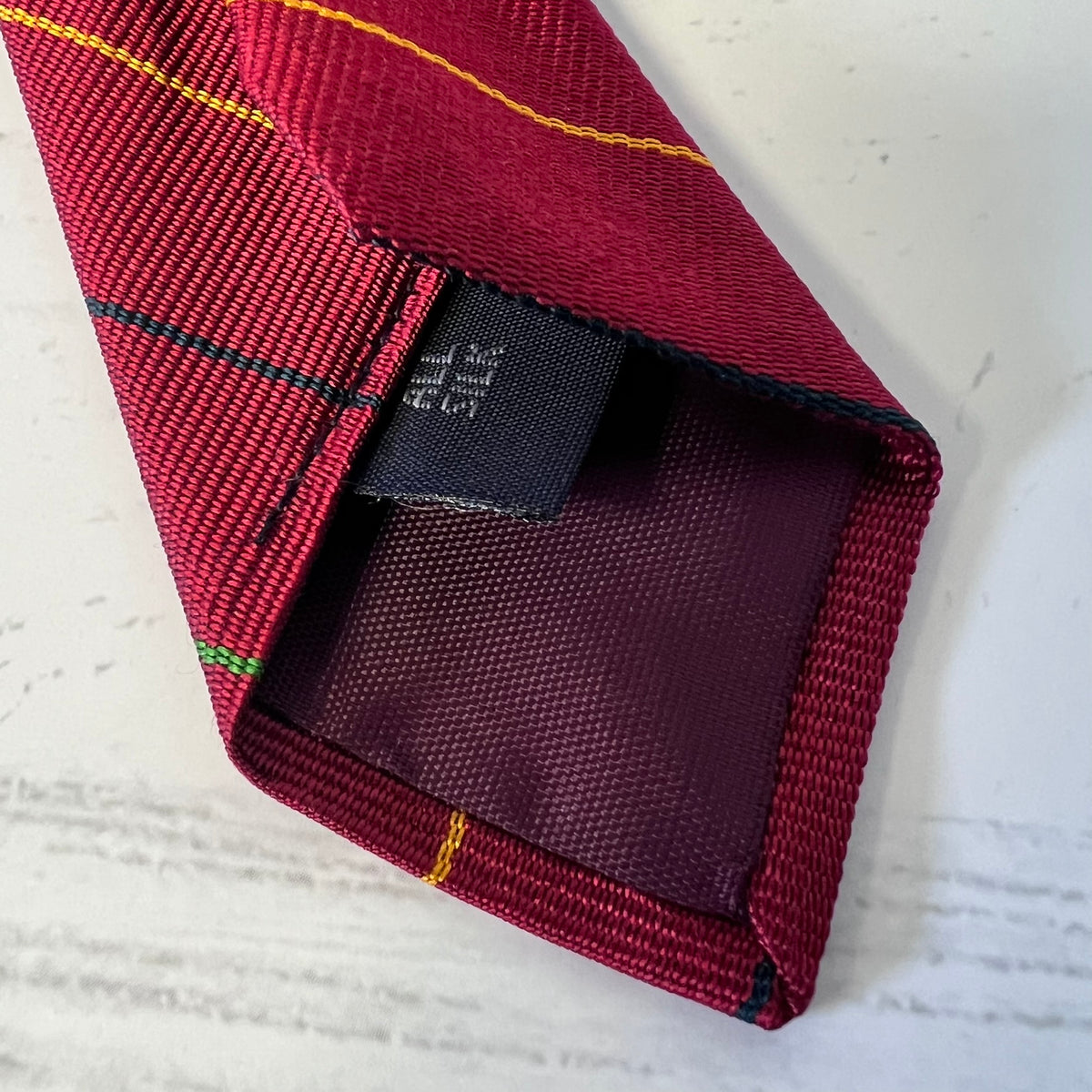 Close-up of a red plaid tie with a brand label on a textured white background