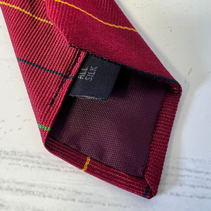 Close-up of a red plaid tie with a brand label on a textured white background
