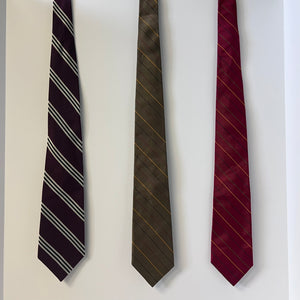 Three striped ties in black, brown, and red on a light gray background