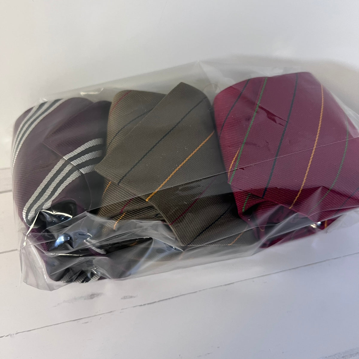 Three striped ties in different colors wrapped in clear plastic on a white surface.