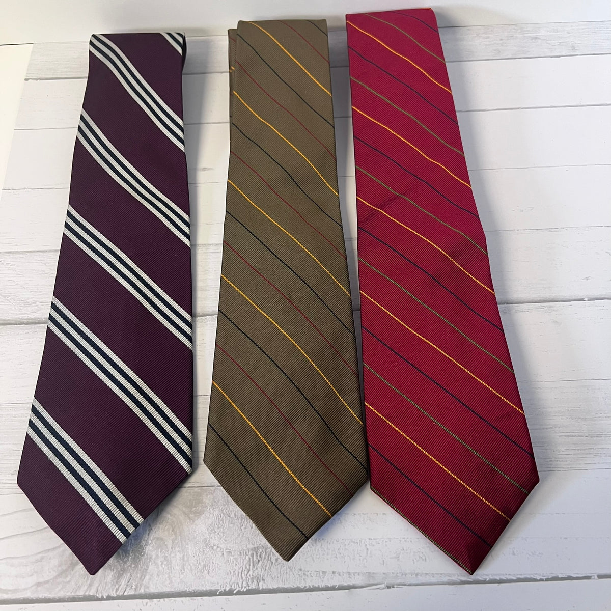 Three striped ties in purple, brown, and red on a light wooden surface