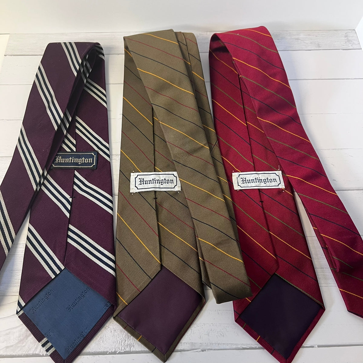 Three striped ties with 'Huntington' branding on a wooden surface