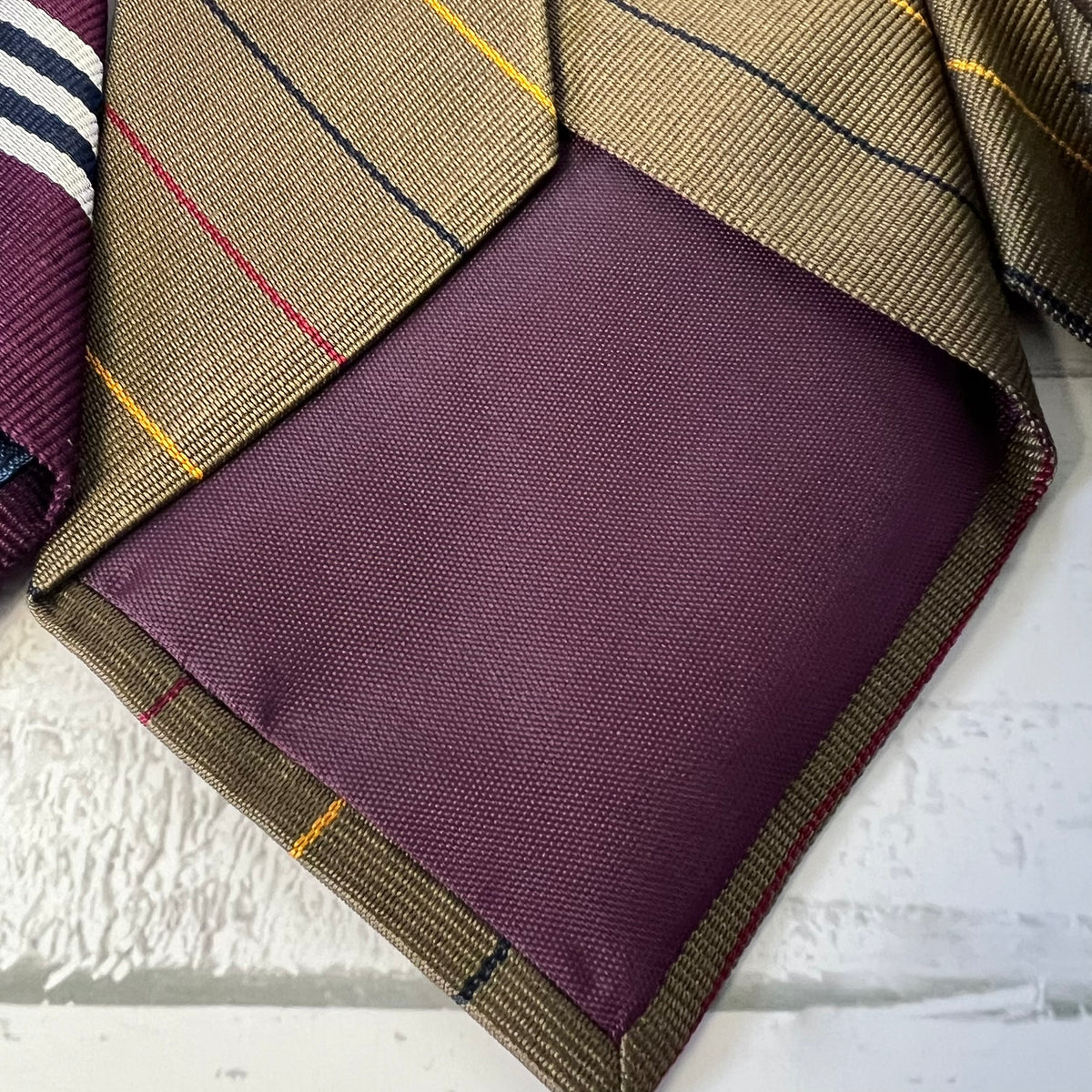 Purple fabric pocket square with plaid border on a textured surface