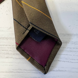 Close-up of a brown woven tie with a purple pocket square on a textured white background