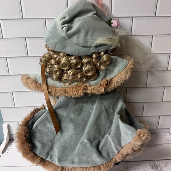 Decorative doll with curly hair and a blue outfit against a white tiled wall.