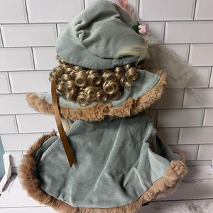 Decorative doll with curly hair and a blue outfit against a white tiled wall.