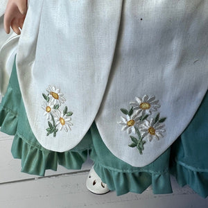 Embroidered floral design on a white fabric with green trim on a wooden floor.