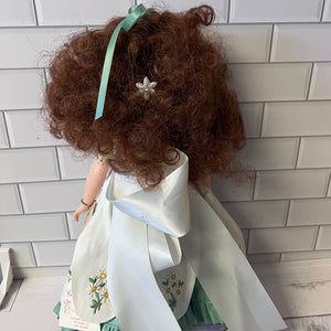 Doll with curly hair and a white outfit against a tiled wall.