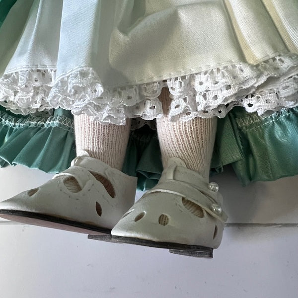 Close-up of a doll's feet wearing white shoes and green ruffled pants on a white background