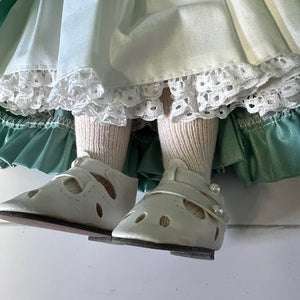 Close-up of a doll's feet wearing white shoes and green ruffled pants on a white background