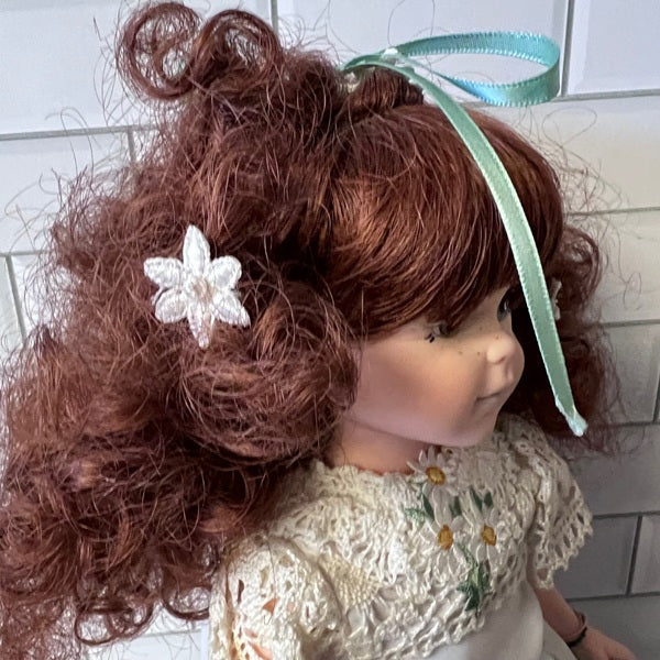 Doll with red hair styled wearing a white lace dress with floral details.