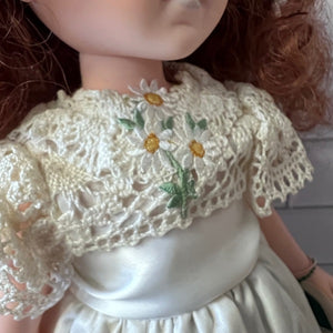 Close-up of a doll wearing a lace shawl with floral embroidery.
