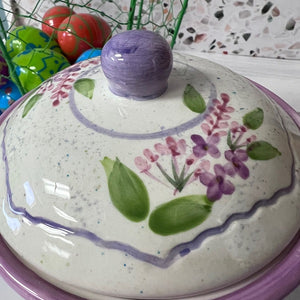 Ceramic lid with floral design and purple handle on a colorful background