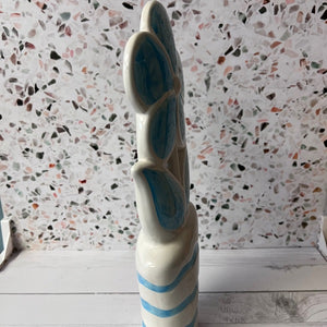 Ceramic vase with blue stripes against a terrazzo-patterned wall.