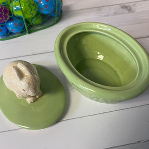 Green ceramic container with rabbit figurine on a white wooden surface