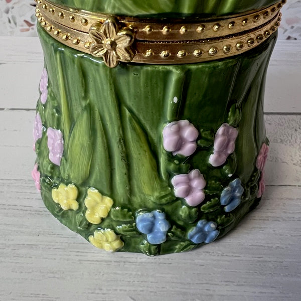 Decorative green container with floral designs and a gold band on a light wooden surface