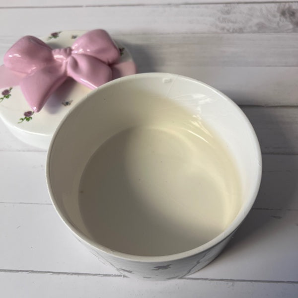 White ceramic bowl on a wooden surface with a pink decorative item in the background