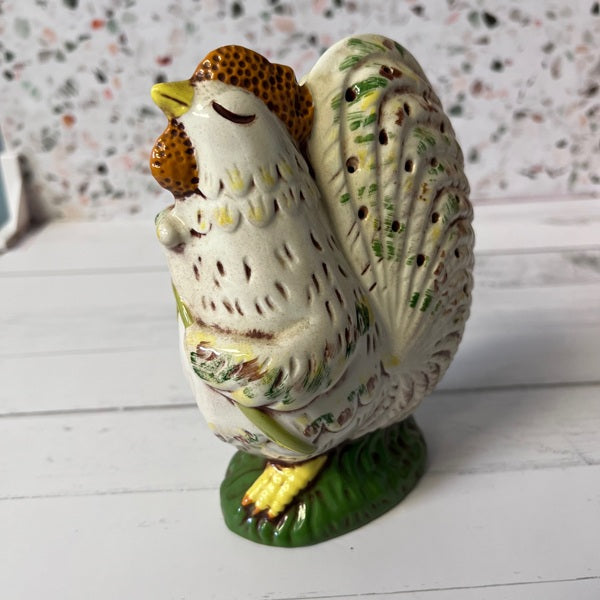 Decorative ceramic chicken figurine on a white surface with a speckled wall background